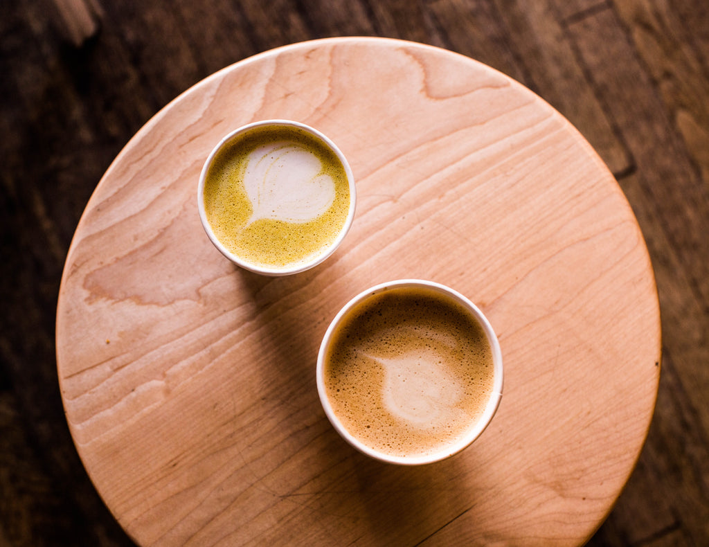 Two cups of cannabis-infused golden milk tea on top of a wooden circular board